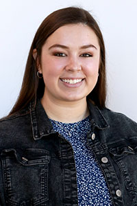 Woman with straight dark hair wearing blue shirt and jean jacket