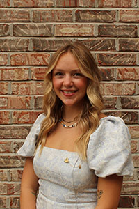 white woman with blonde hair standing in front of brick wall smiling