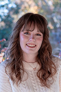 woman with red-brown hair wearing a cream sweater smiling