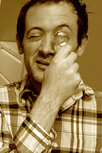 man with dark hair using a magnifying glass wearing a plaid shirt. Photo has brown antique color