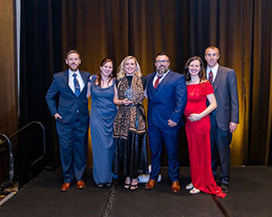 Blonde woman in formal wear holding award posing with others in formal wear