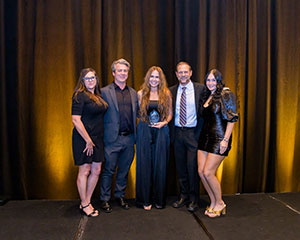 White woman long red hair holding award standing with others in formal wear.