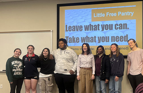 group of students standing in front of projector with their professor