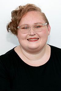 person with short strawberry blonde curly hair wearing glasses and a black shirt